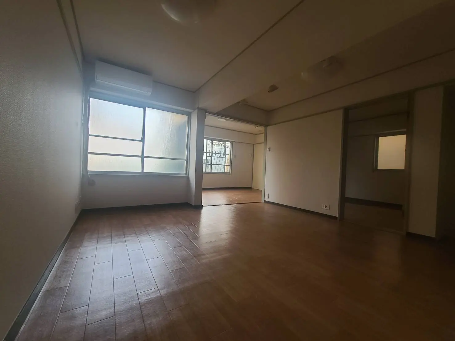 広々とした空の部屋と木製フローリング、バルコニーへの出入り口がある明るい日差しのアパート내부