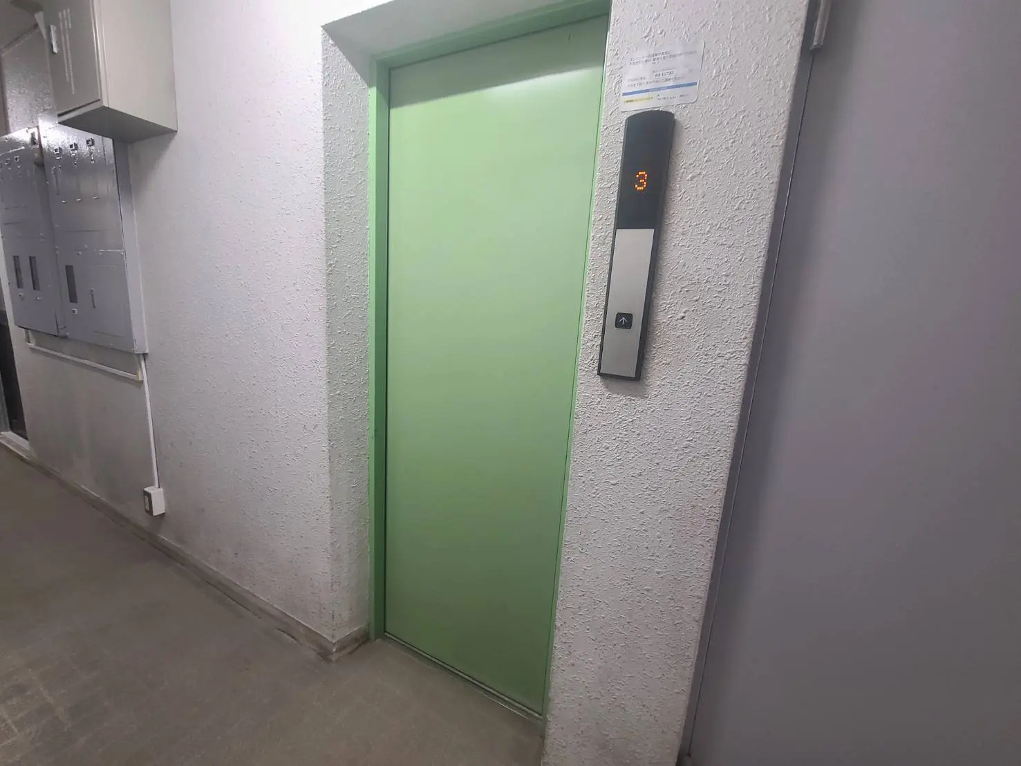 建物内の緑色のエレベーター扉と隣に表示板がある通路