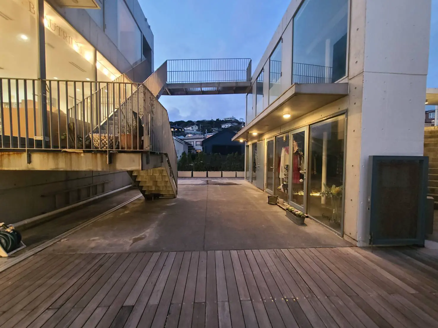 夕暮れ時のモダンな建築スタイルの建物の外観、ガラス張りのファサードと木製デッキ、階段と橋のディテール