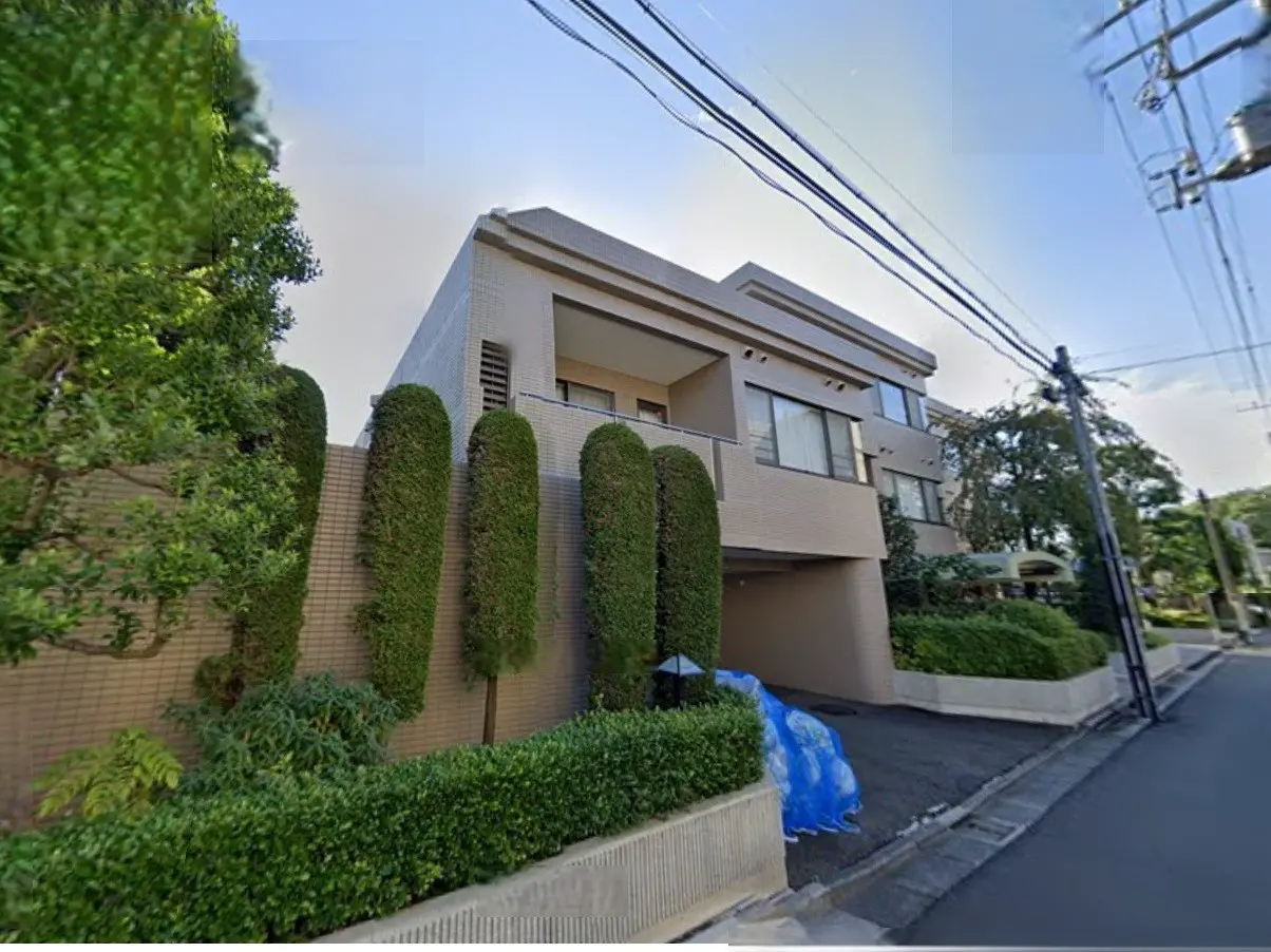 - モダンスタイルの住宅外観、高い生垣と整えられた植栽、明るい空の下にある建物と駐車スペース