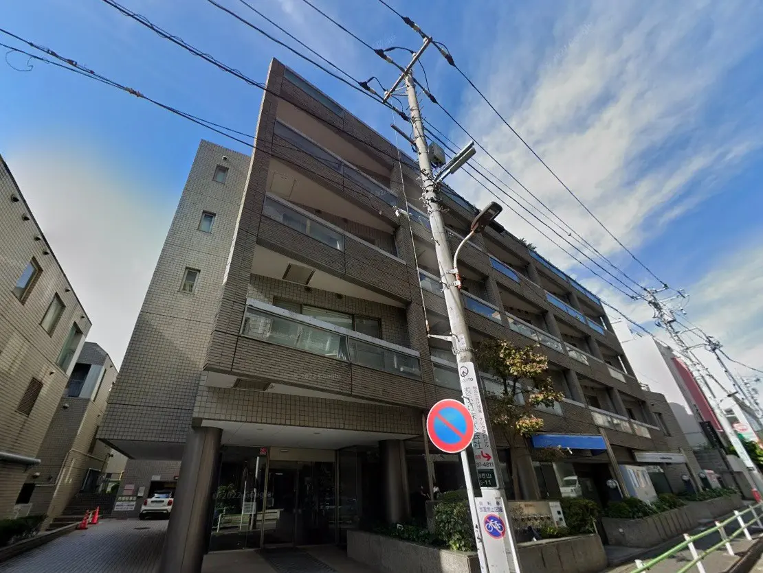 現代的な外観の都市型マンション、入り口に看板、青空と電線が見える街並み