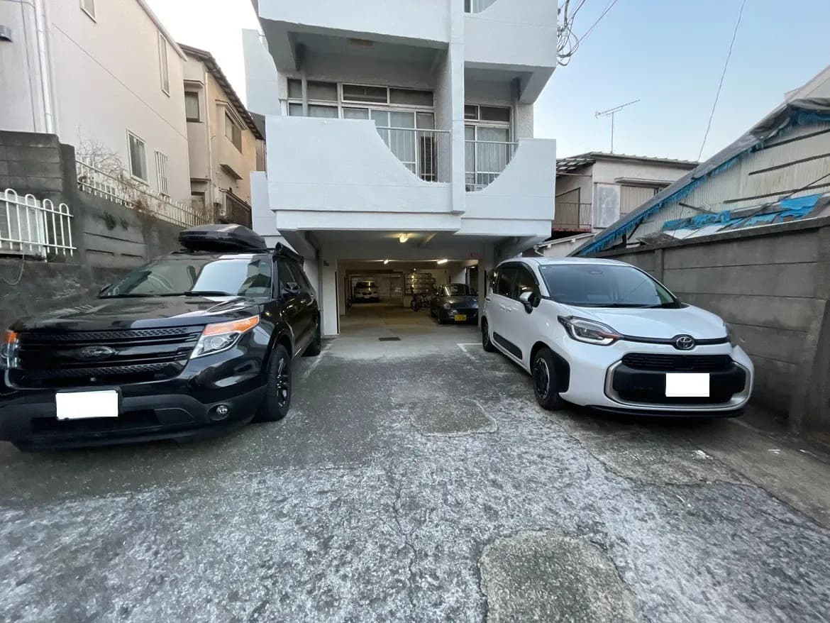 都市の居住エリアに駐車された2台の車、建物のカーポートが見える外観