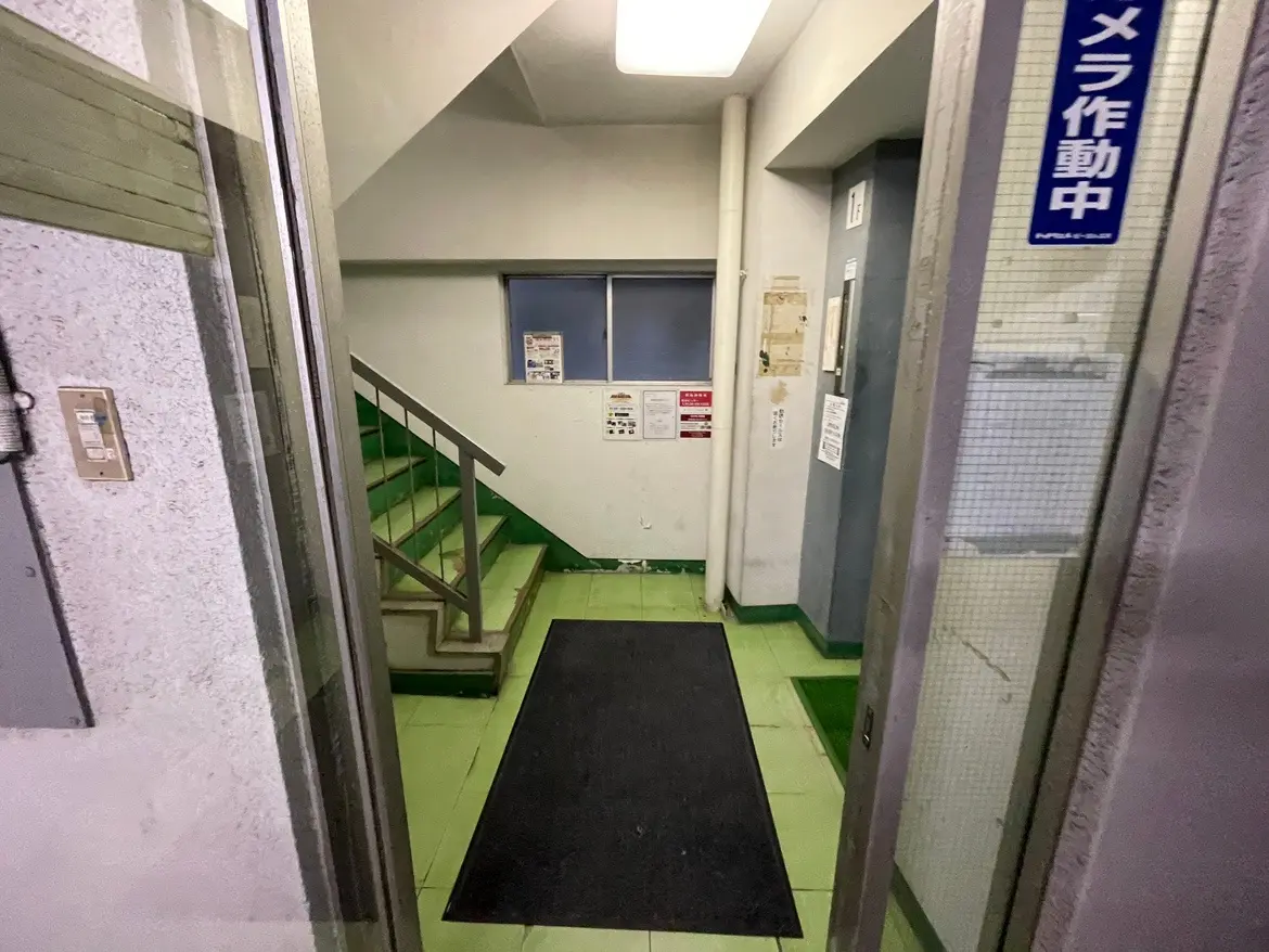 古いマンションの共用エントランス、階段とエレベーター、メールボックスが見える廊下