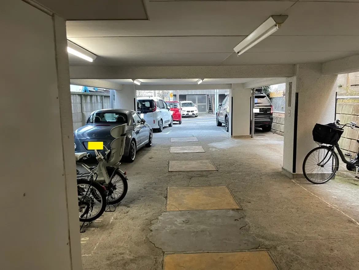 屋根付きの駐輪スペースがある都市のアパート駐車場、コンクリートの建物と自転車、背景に車両が見える