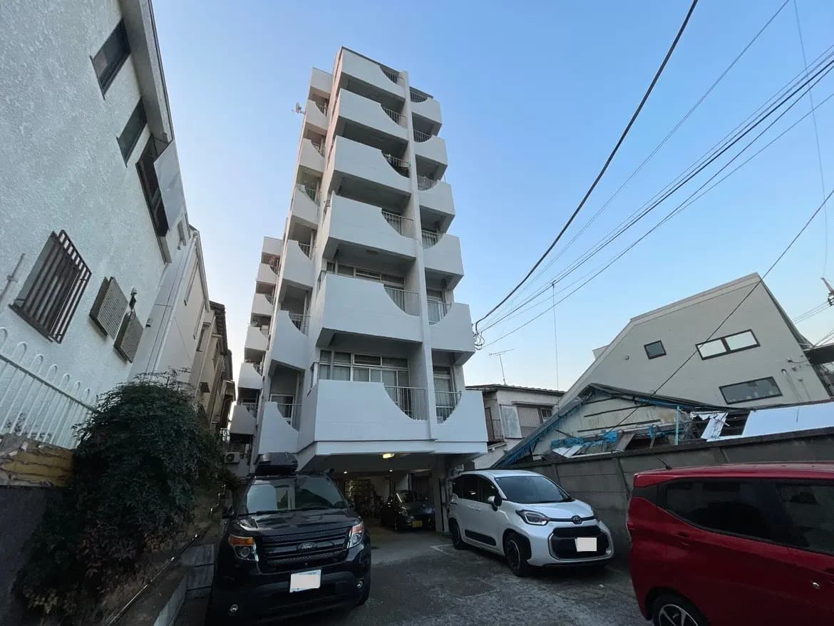 都市の住宅地にある白い多階建てアパートと駐車された車들