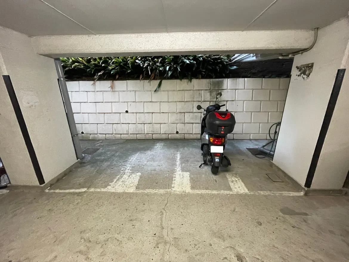 駐車場に停められたスクーター、白い壁と緑の植栽が見える都市の屋内ガレージ