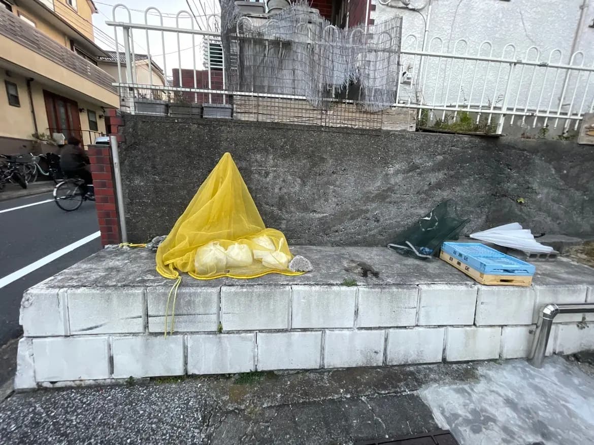 街中のブロック塀にかけられた黄色いネットと捨てられたダンボール、衛生的な手入れが必要な公共スペース