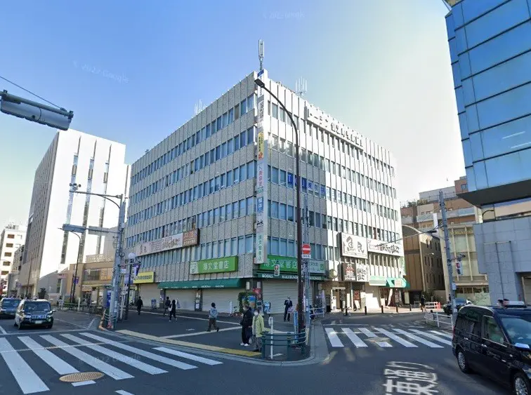 交差点に位置する現代的なビル、鮮やかな青空と活気ある街角、看板が目立つ外観