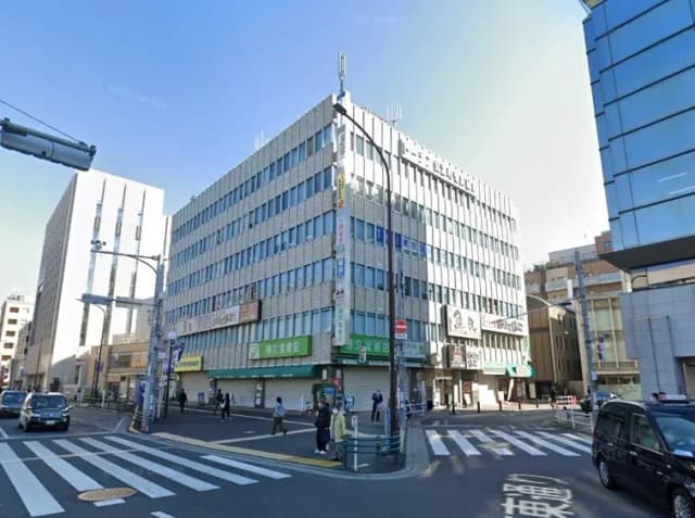 交差点に位置する現代的なビル、鮮やかな青空と活気ある街角、看板が目立つ外観