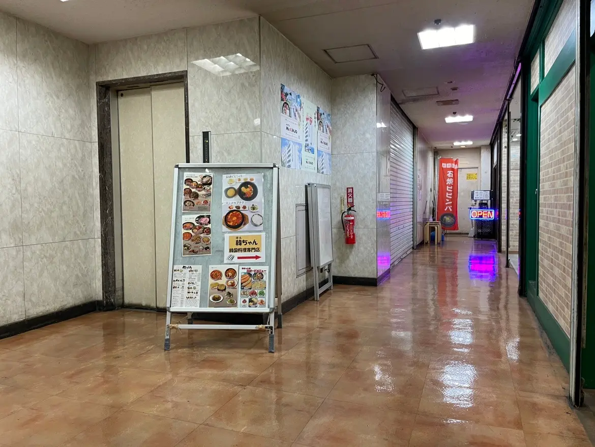 ビル内の通路とレストランのメニュー看板、ピンクの照明が映るタイルの床