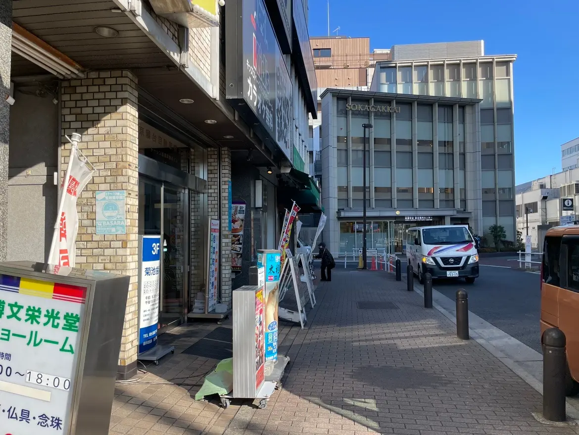 日本の都市の通りの風景、明るい天気の下での店舗と歩行者、後方に見えるビルと駐車している車