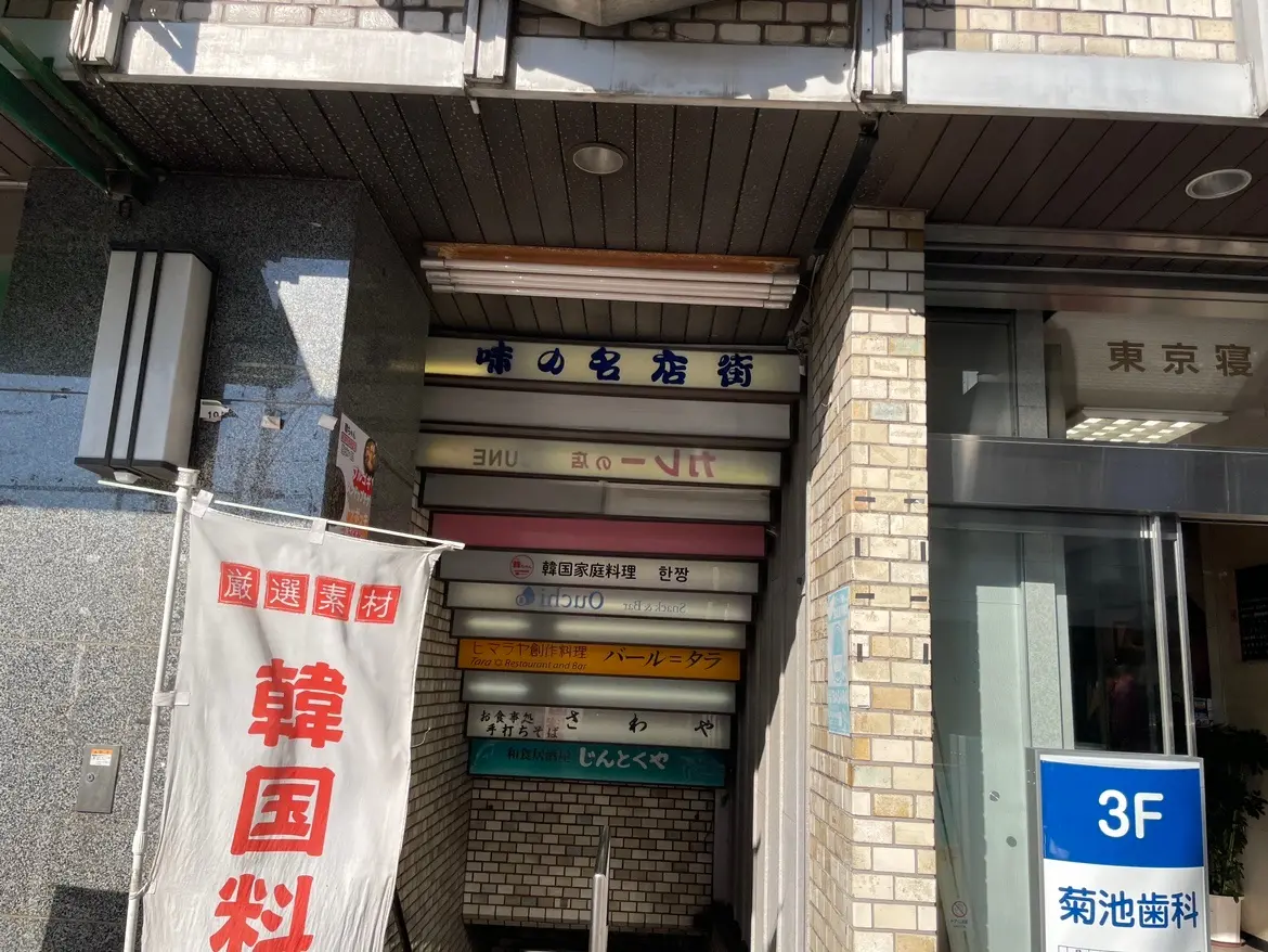 日本の街角にある多様な店舗の看板が並ぶビルの入り口、日中の都市風景