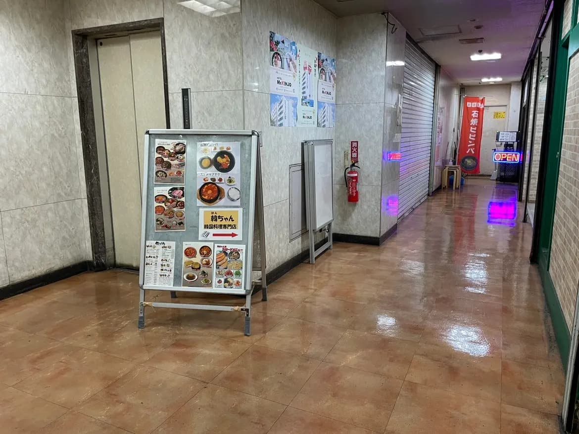 日本のアーケード内にある食品メニュー看板が置かれた通路、ピンク色の照明、レストランへの案内表示