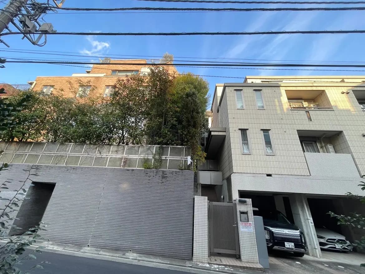 都市の住宅街にある建物と駐車場、背景には樹木と青空