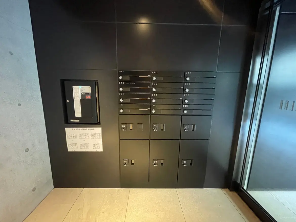 現代的なマンションのエントランスホールに設置された郵便受けとインターホン、グレーの壁とタイルフローリング