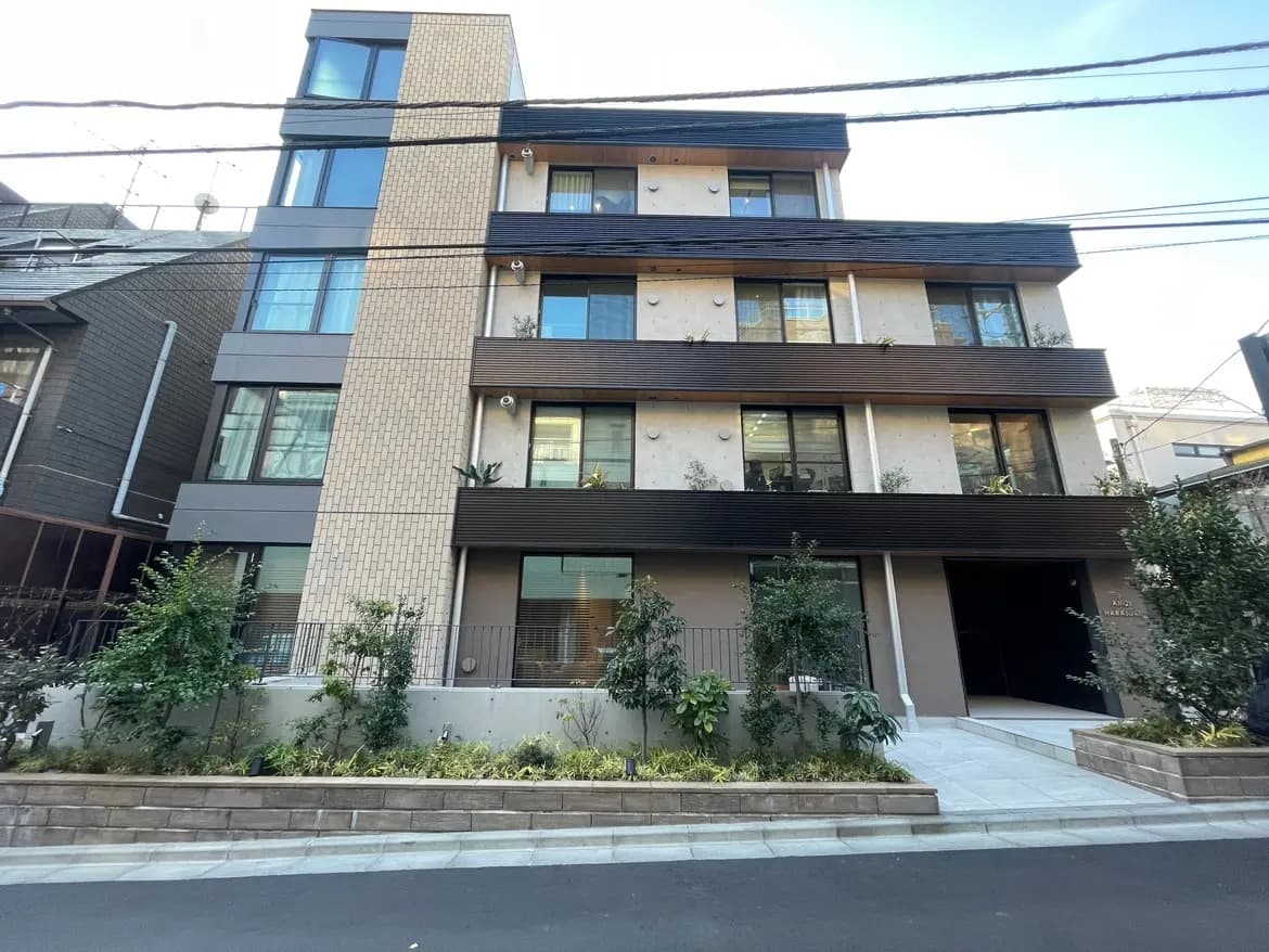 現代的なデザインのマンション外観、ベージュとダークブラウンの外壁、街路樹と植栽が美しい住宅街
