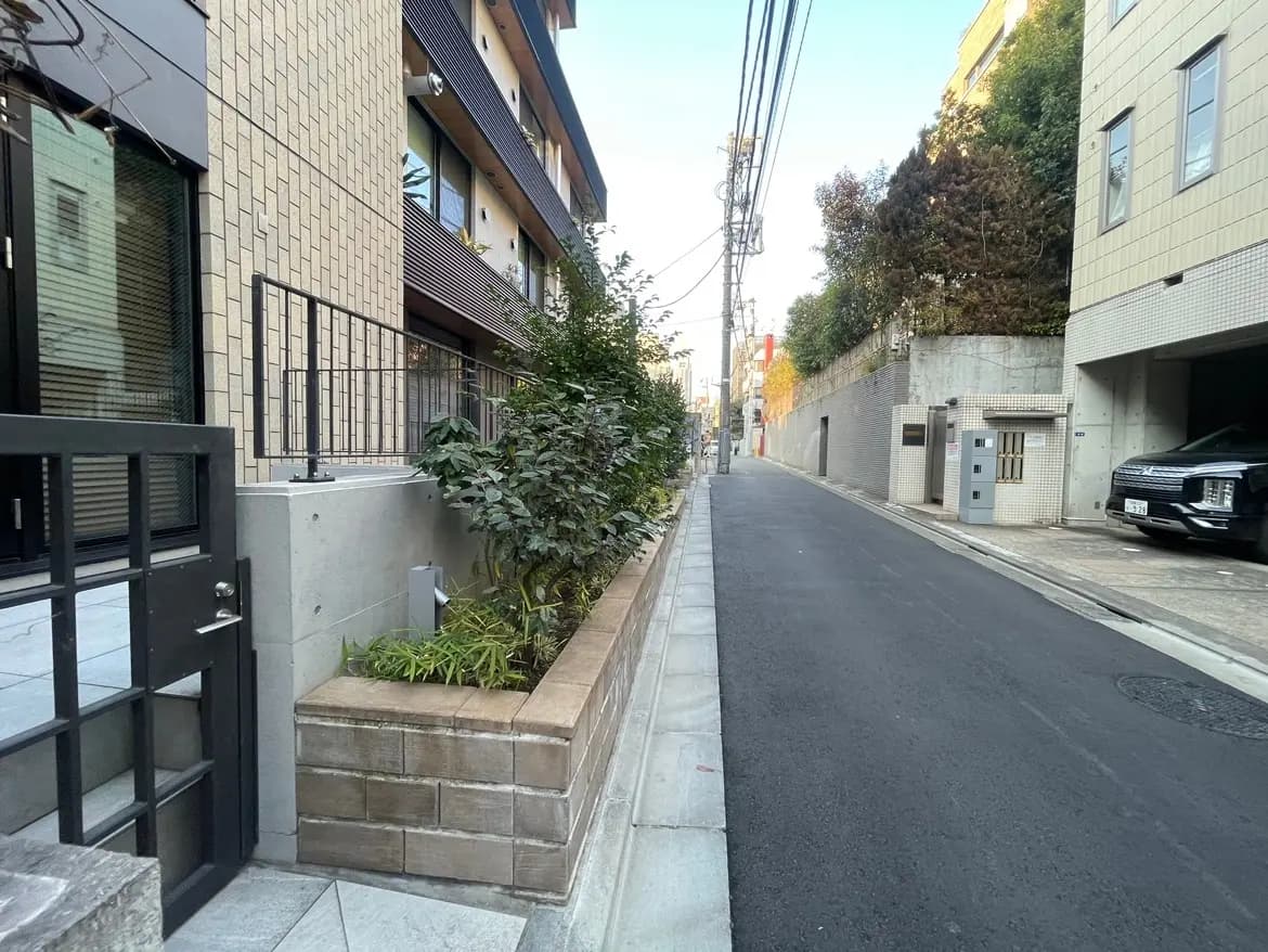 都市の住宅地にあるモダンなアパートメント、整備された街路と植栽、午後の日差し
