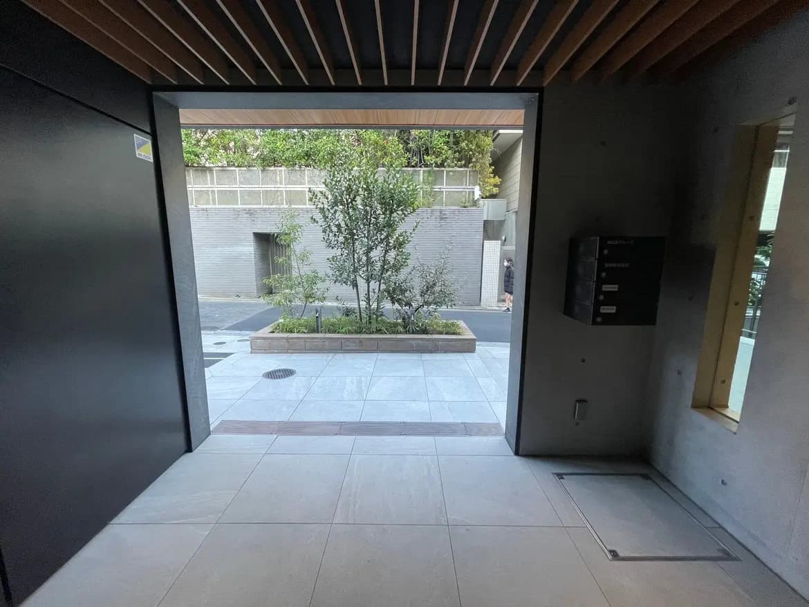 現代的なデザインのエントランスホール、天井の木目調ディテール、外の緑の木、明るい日差しが差し込む