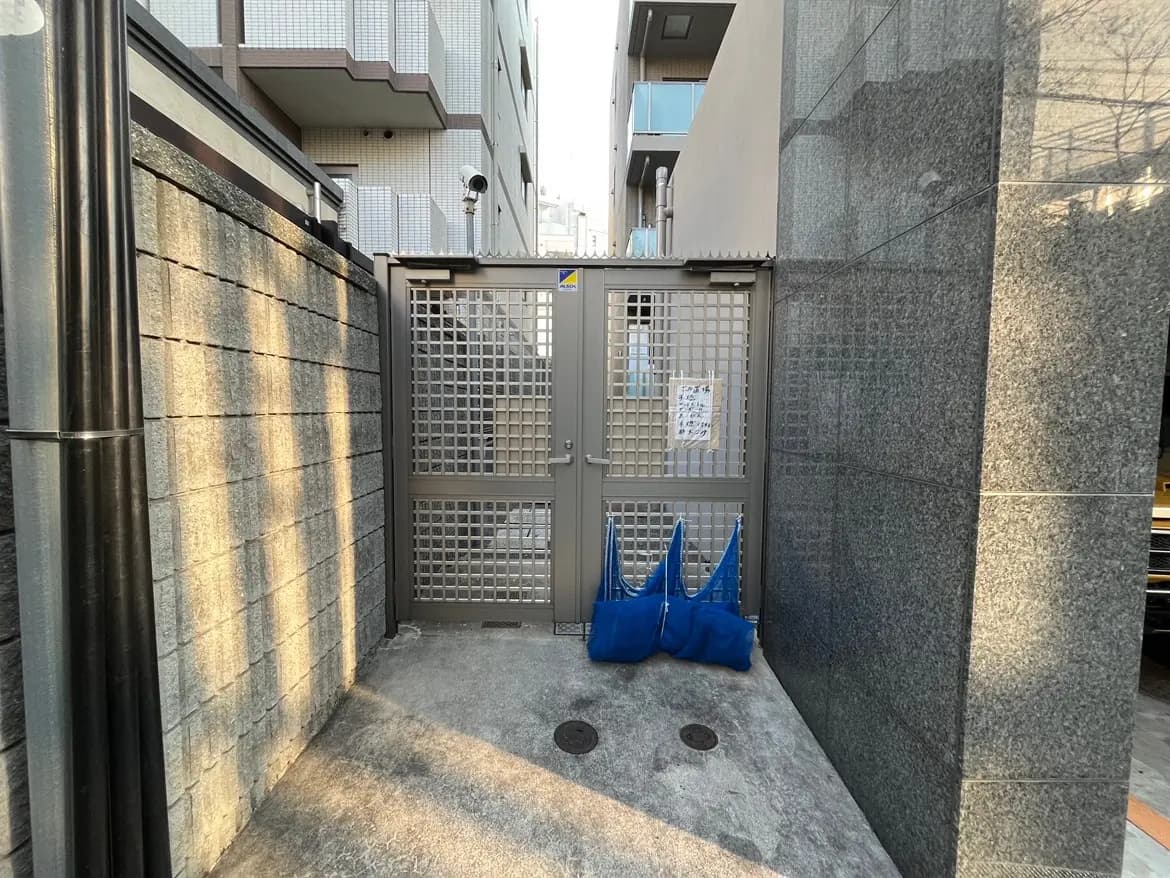 市街地にある建物のエントランスゲート、グレーの壁と黒い柵、ブルーのビニール袋が置かれている外観