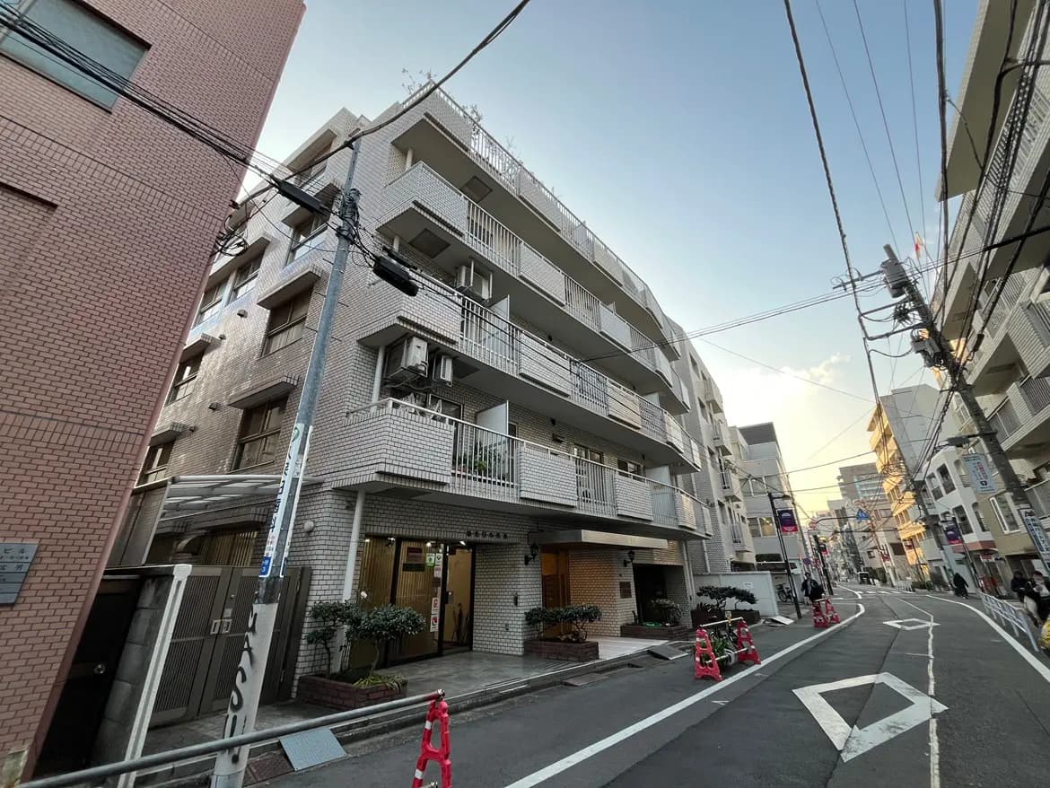 都市の住宅街に位置する現代的なアパート建物、晴れた日の青空、通り沿いの電柱と配線