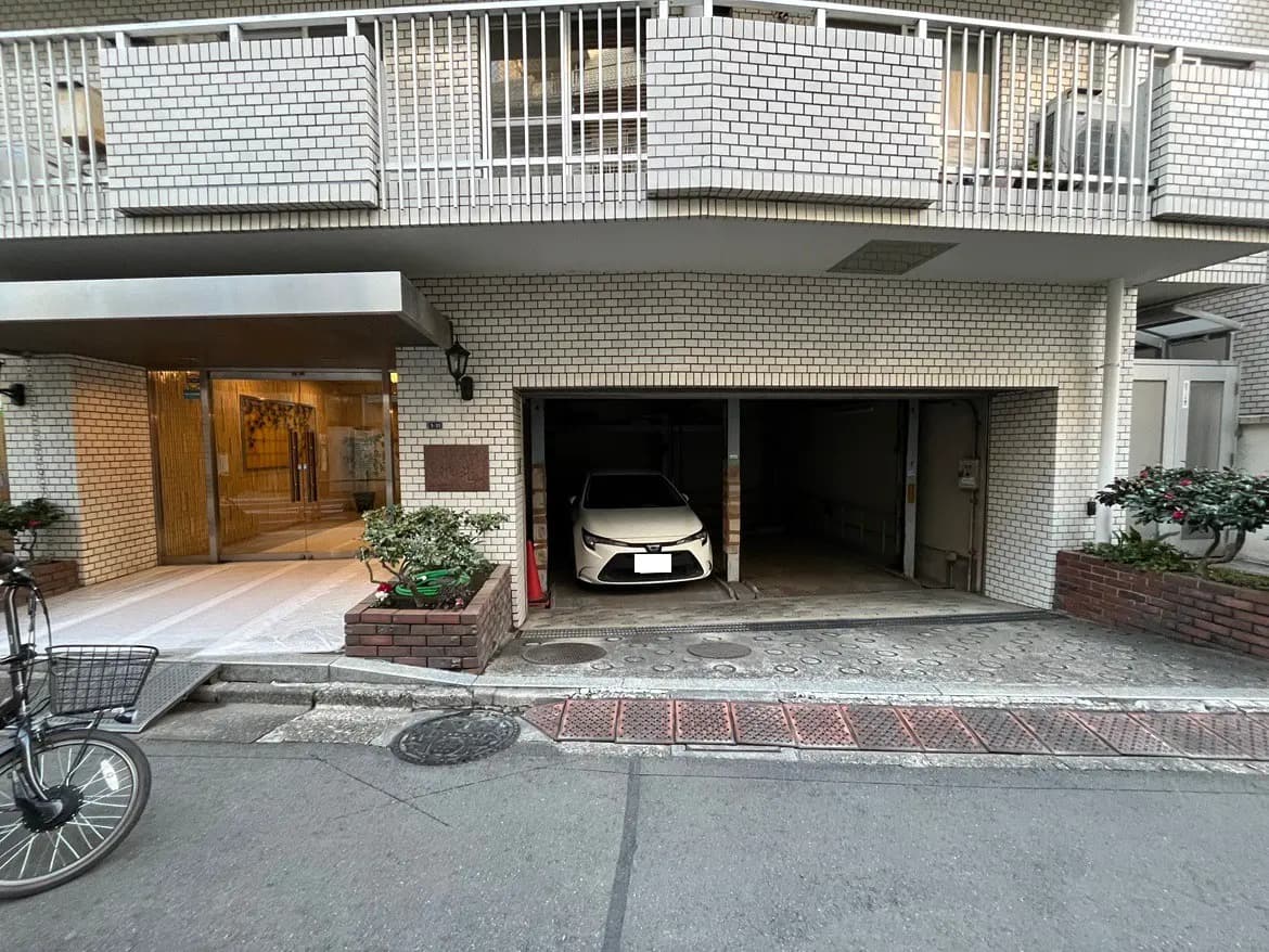 都市の集合住宅のエントランスと駐車スペース、自動車が停まっている外観