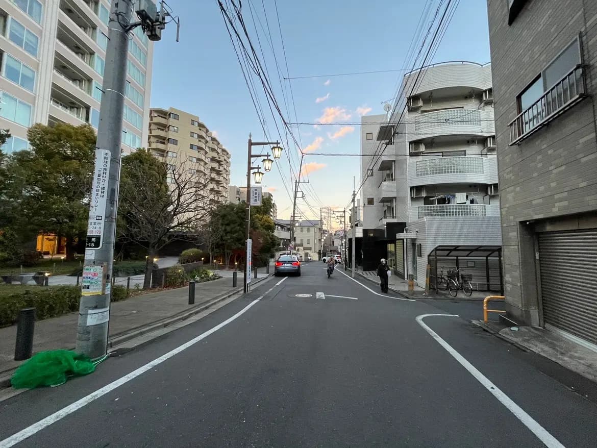夕暮れ時の日本の都市風景、アパートやビルが立ち並ぶ静かな住宅街、歩道と道路に見える電柱と配線