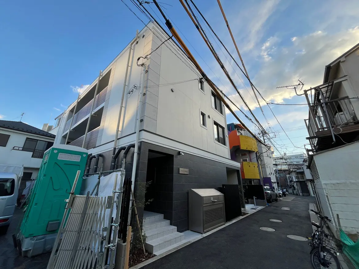現代的な外観の都市住宅、青空に向かって伸びる電線、狭い通りに駐車した車と自転車