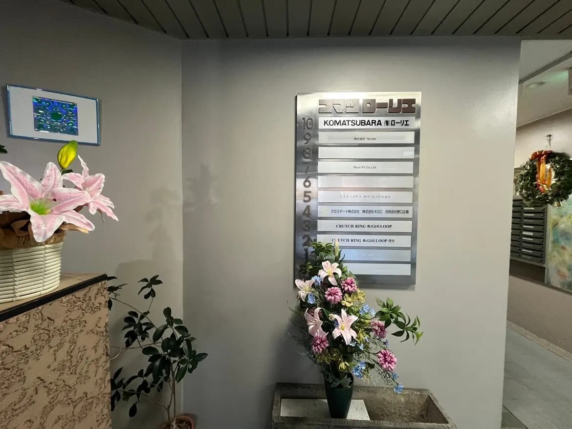 オフィスビルのエントランスに表示されているテナント案内ボード、装飾された生花と観葉植物