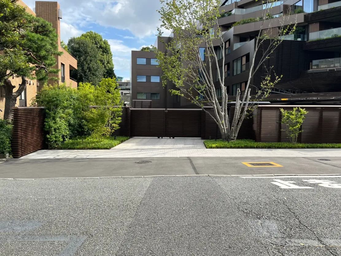 - 都会の住宅地にあるモダンな建物の外観、緑豊かな植栽と整備されたアプローチ、洗練されたフェンスが特徴の風景