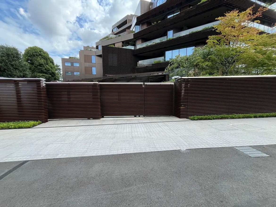 - モダンなデザインの建物の前にある木製のスラットフェンス、青空と周囲の緑と調和した景観