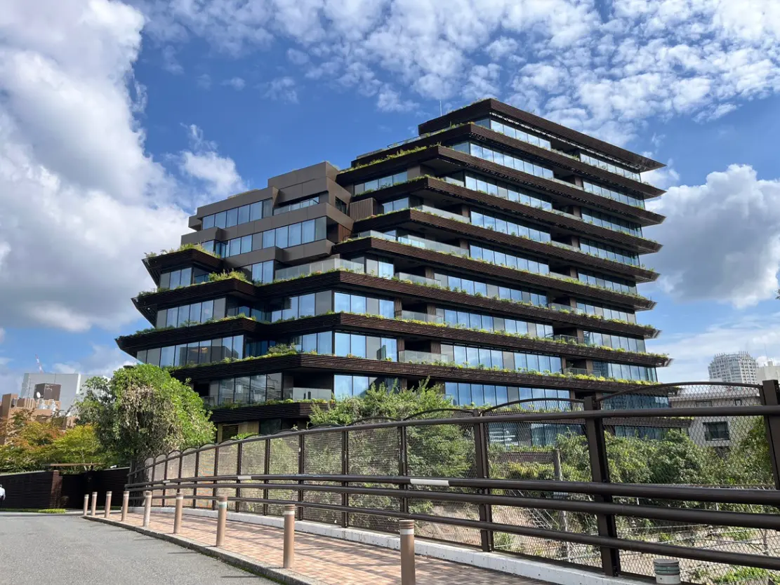 - 植栽が施されたモダンなオフィスビル、青空と白い雲を背景にしたギザギザの外観デザイン