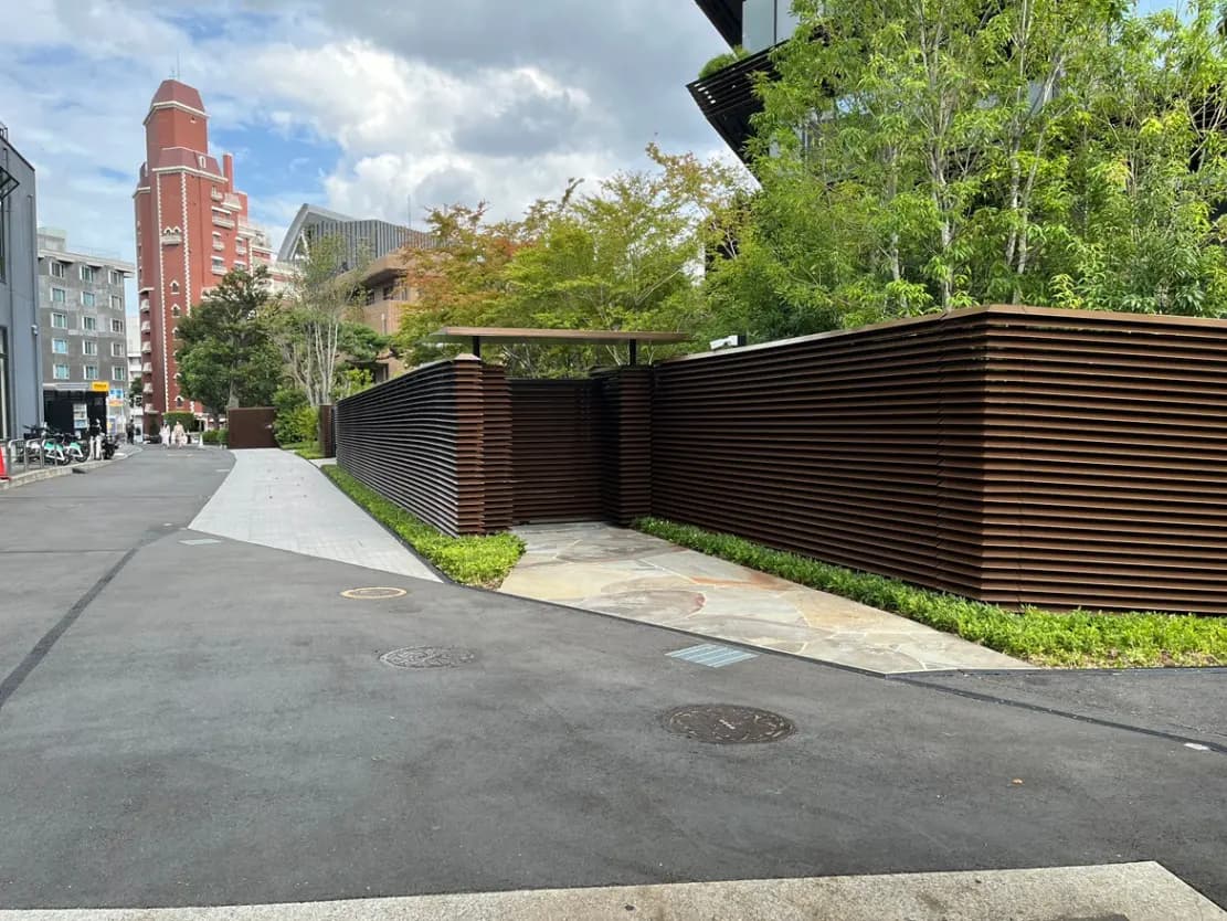 - 現代的なデザインの囲いが施された道、右側には緑豊かな植栽と整備された歩道が続く風景