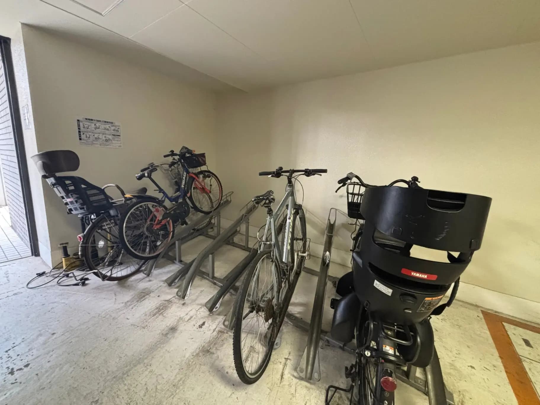 駐輪スペース内に並ぶ様々な自転車と電動スクーター、コンクリートの床と白い壁の都市的な環境