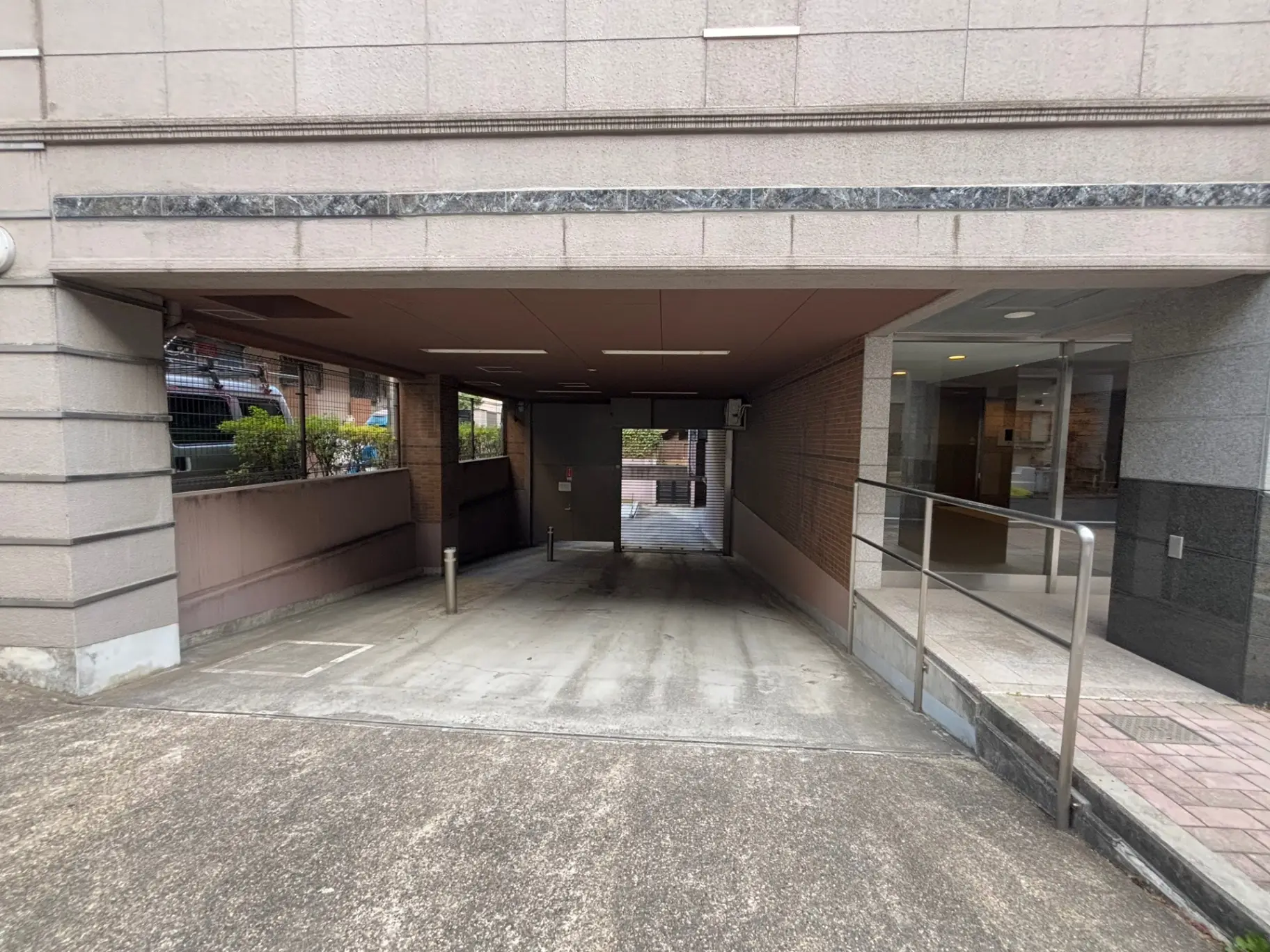 現代的な外観の建物入口、屋根付き駐輪スペース、ガラス扉と手すりが見える通路