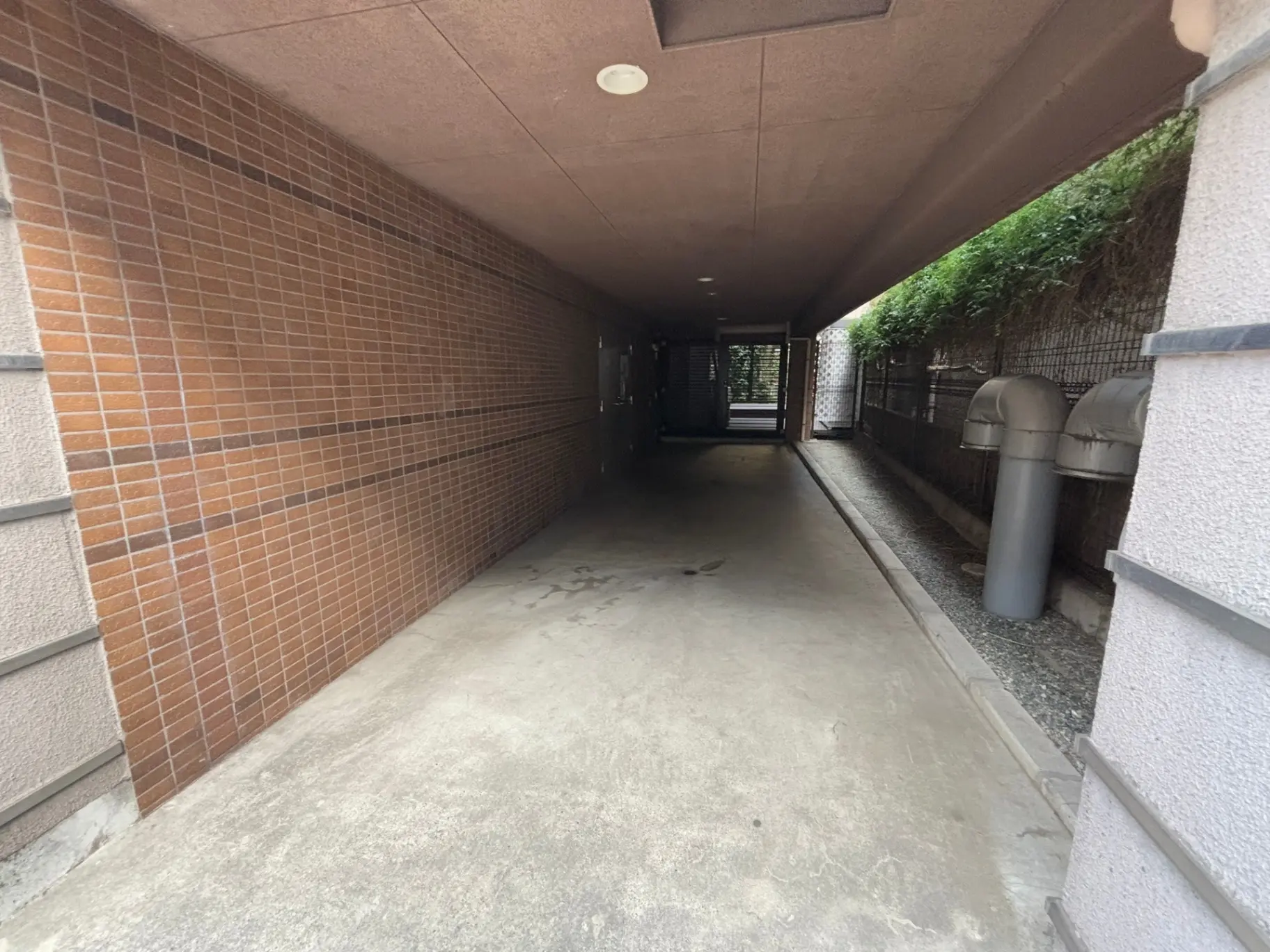建物の外廊下、赤茶色のタイル壁面とコンクリートの床、天井に埋め込み型照明が設置された通路