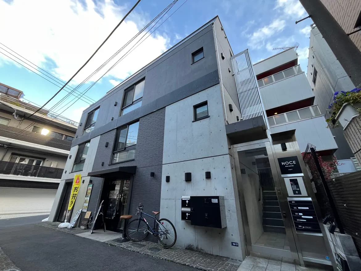 - 現代的なデザインの二階建てビル、コンクリートとタイルの外観、エントランスには自転車と看板がある街並みの風景