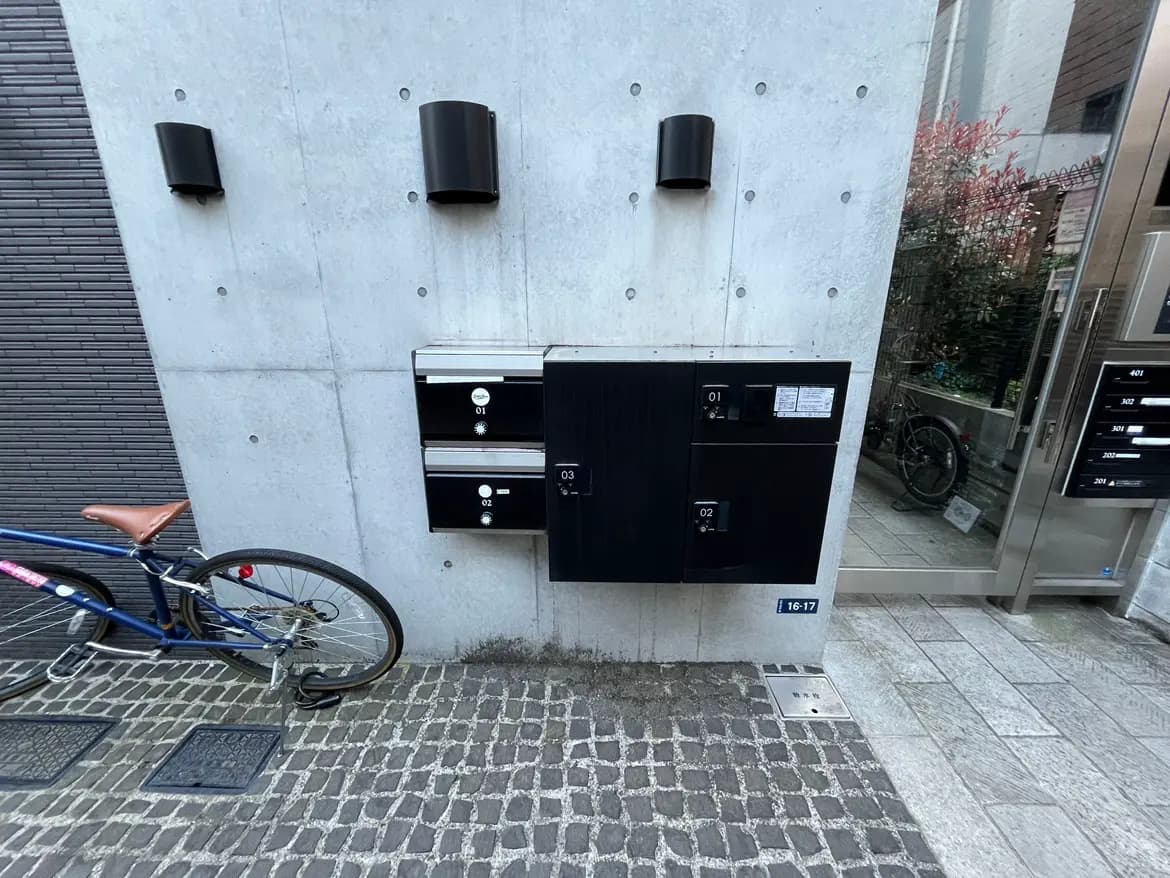 - モダンなコンクリート壁に取り付けられた郵便受け、隣には自転車が停まっている、整然としたエントランスの風景