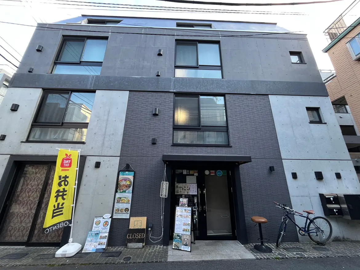 - モダンな外観のレストランビル、黒いタイルの壁と大きな窓、テイクアウトの看板が目立つ入り口の様子