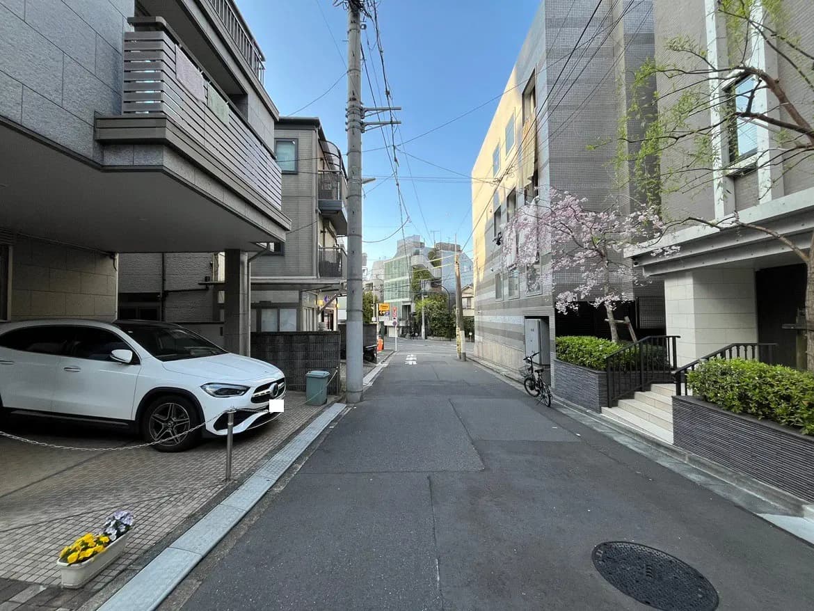 - 都市の住宅街の風景、白いSUVと桜の木がある静かな通り、近代的な建物が立ち並ぶ街並み