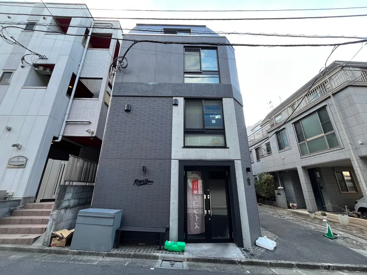 - モダンな外観のアパート、グレーのタイルとコンクリートの壁、隣接する建物との間口が狭い立地