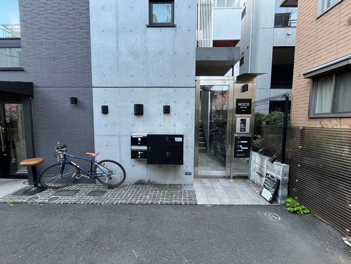 - モダンな外観の集合住宅前に置かれた自転車と郵便受け、ガラスのエントランスが見える通りの風景
