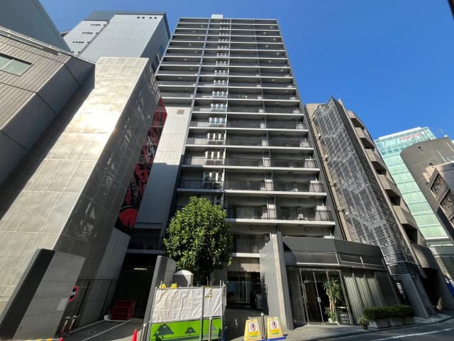 - 現代的な外観のマンションビル、青空を背景にした高層建築物、周辺に緑と街の風景が広がる