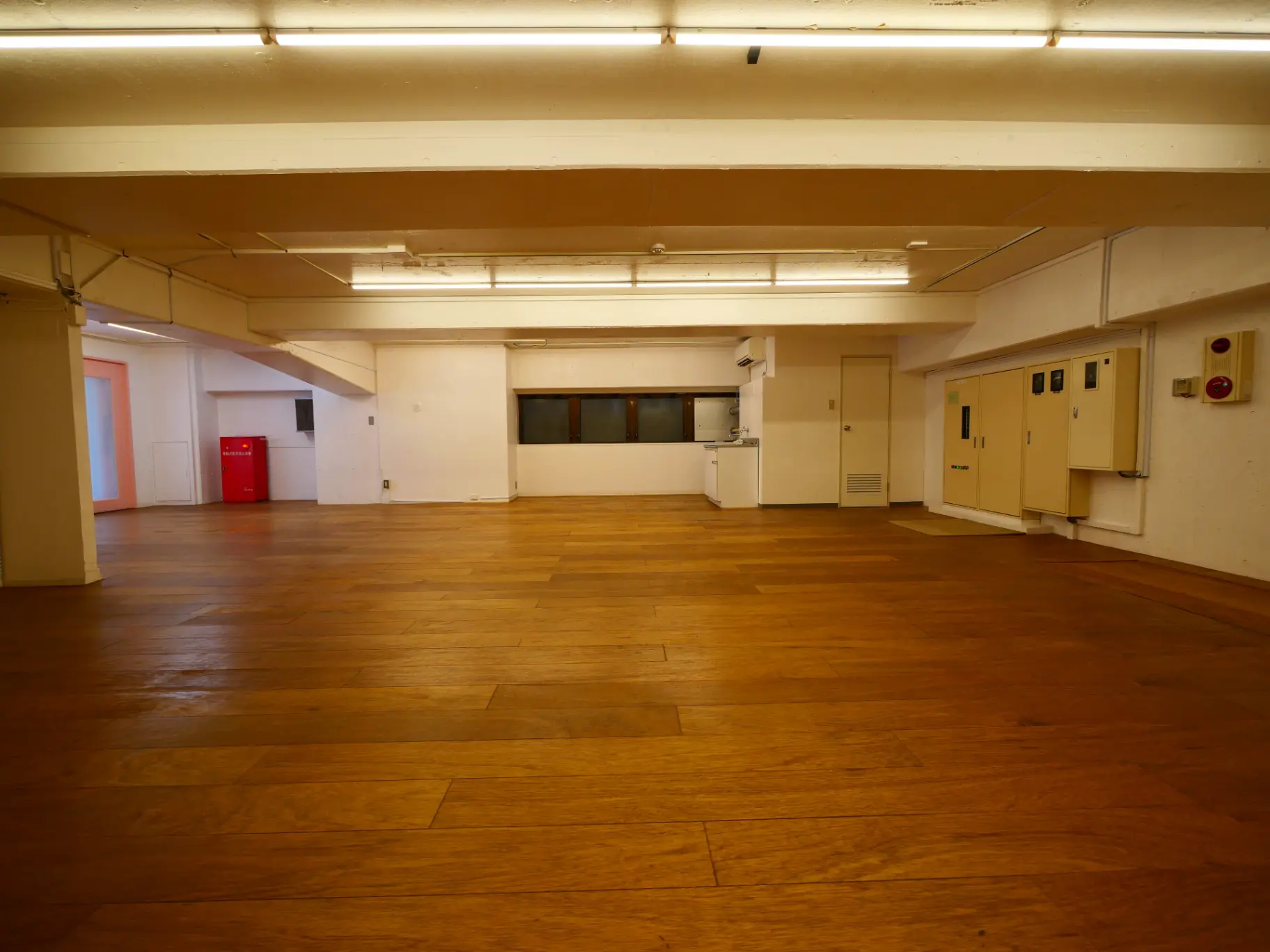 広々とした空間の木製フローリング、白い壁、天井に照明が備えられた多目的ホール
