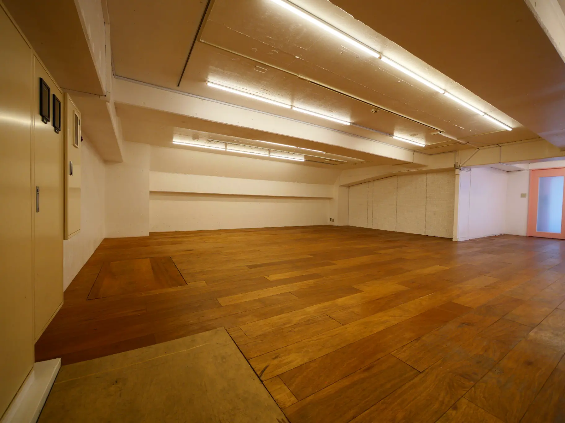 広々としたダンススタジオまたはワークショップスペース、木製フロアと白い壁、天井にはライトが備えられたインテリア