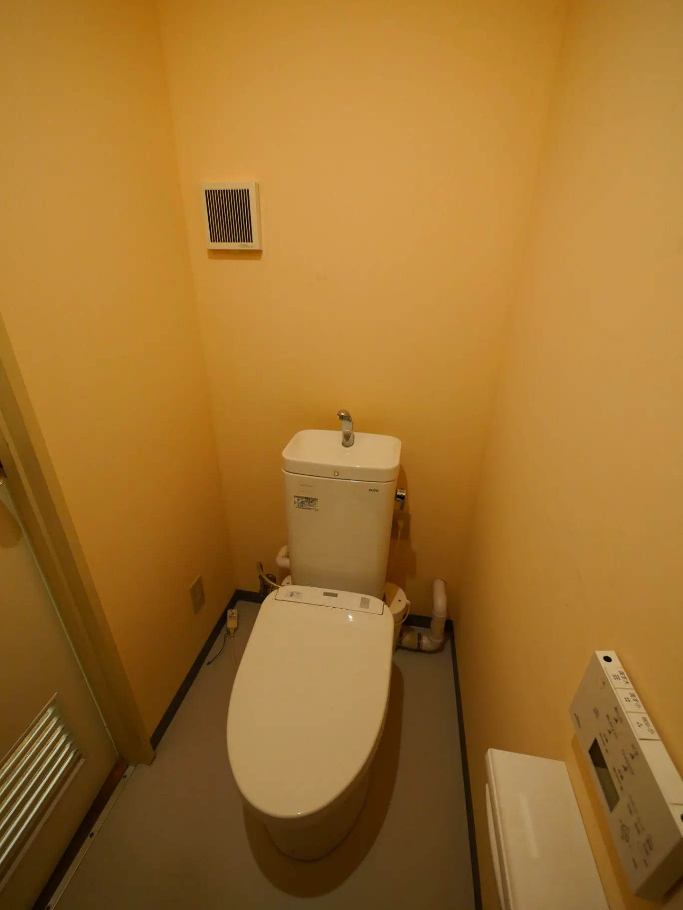 シンプルなデザインのトイレルーム、ウォシュレット付き便器と暖房器具、クリーム色の壁