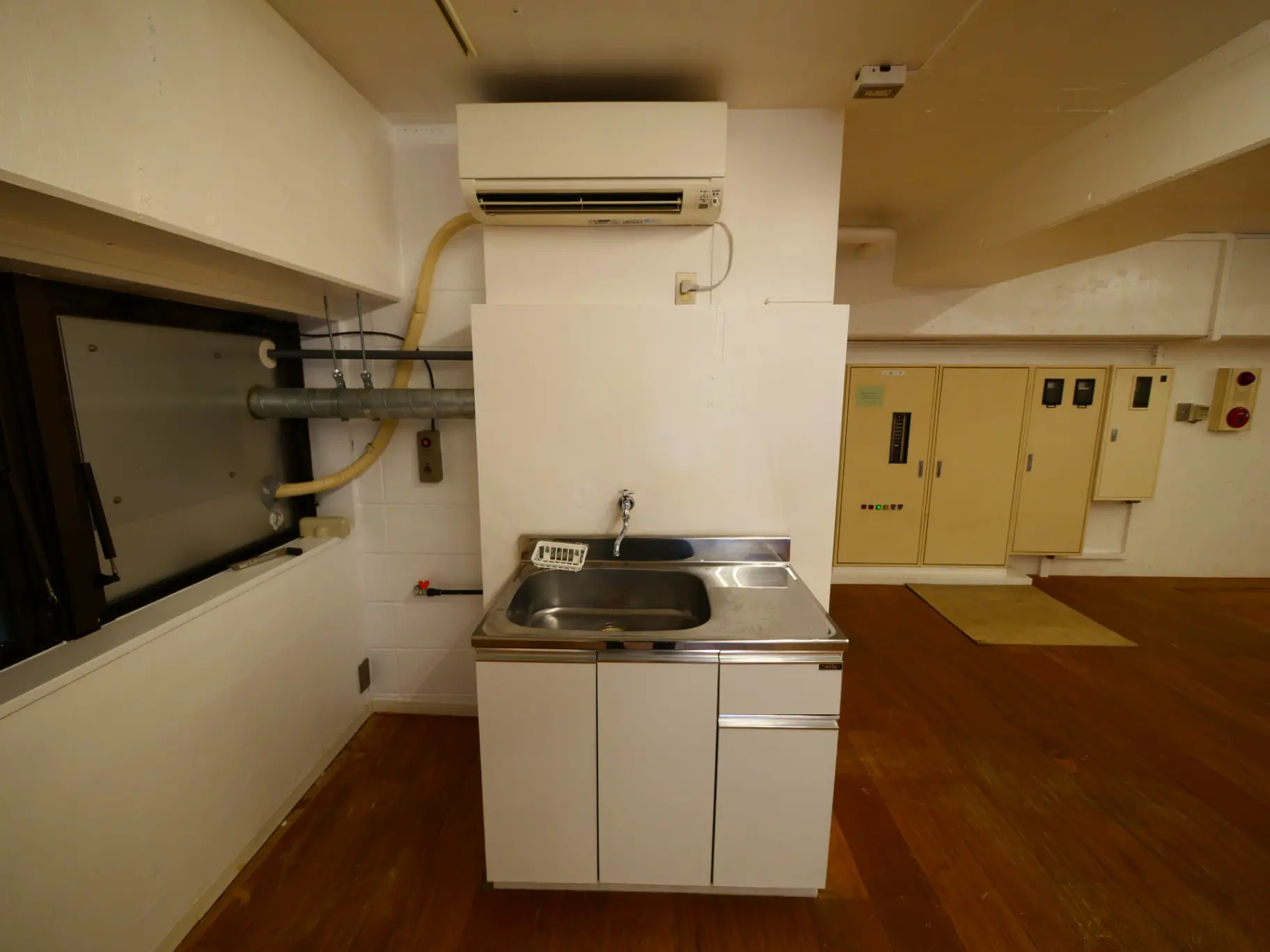 コンパクトなキッチンスペース、ステンレス製シンクと白い収納キャビネット、床は木製フローリング