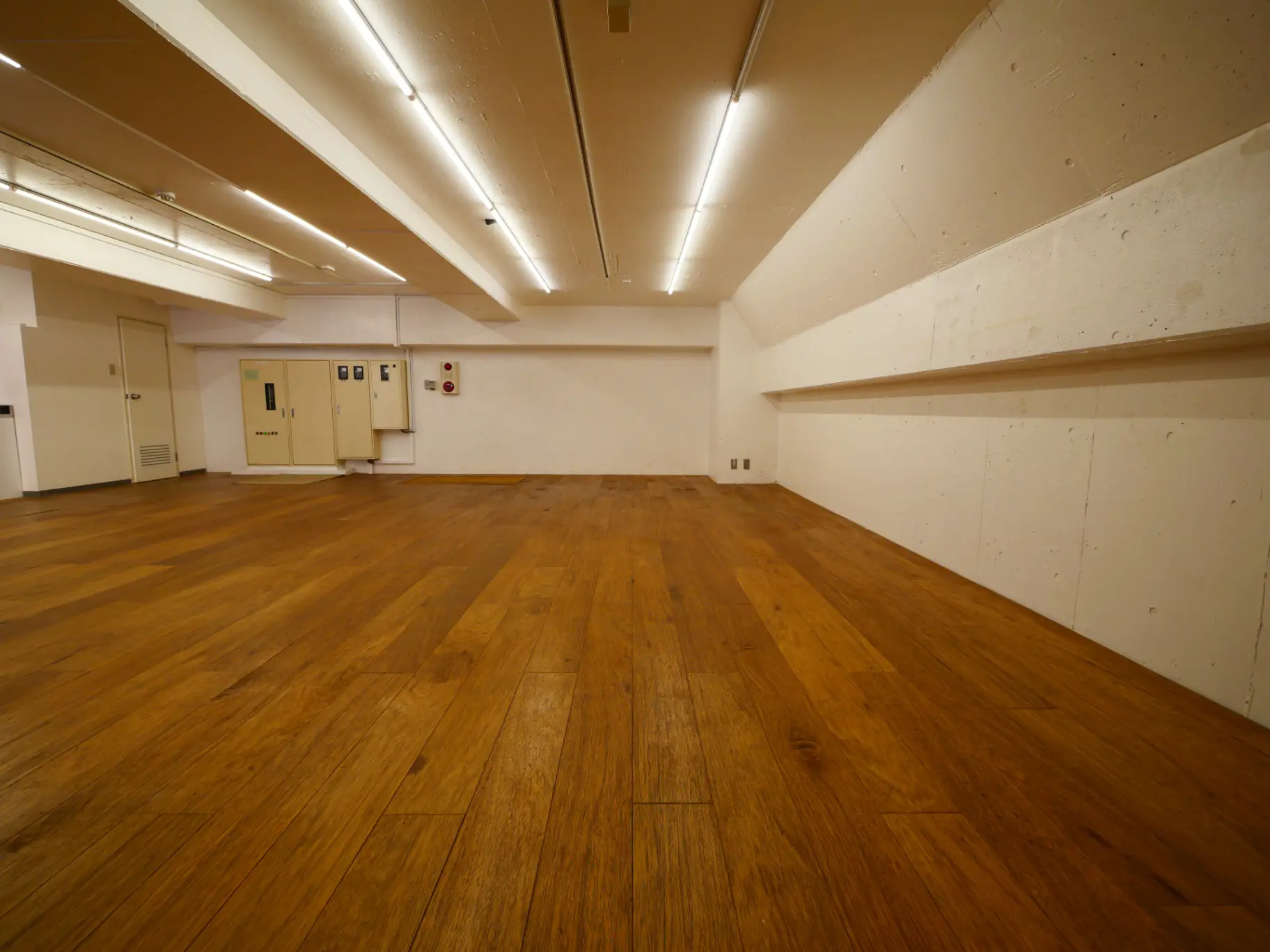 広々とした空間のダンススタジオ、木製フロア、明るい照明、ミラーなしの練習場