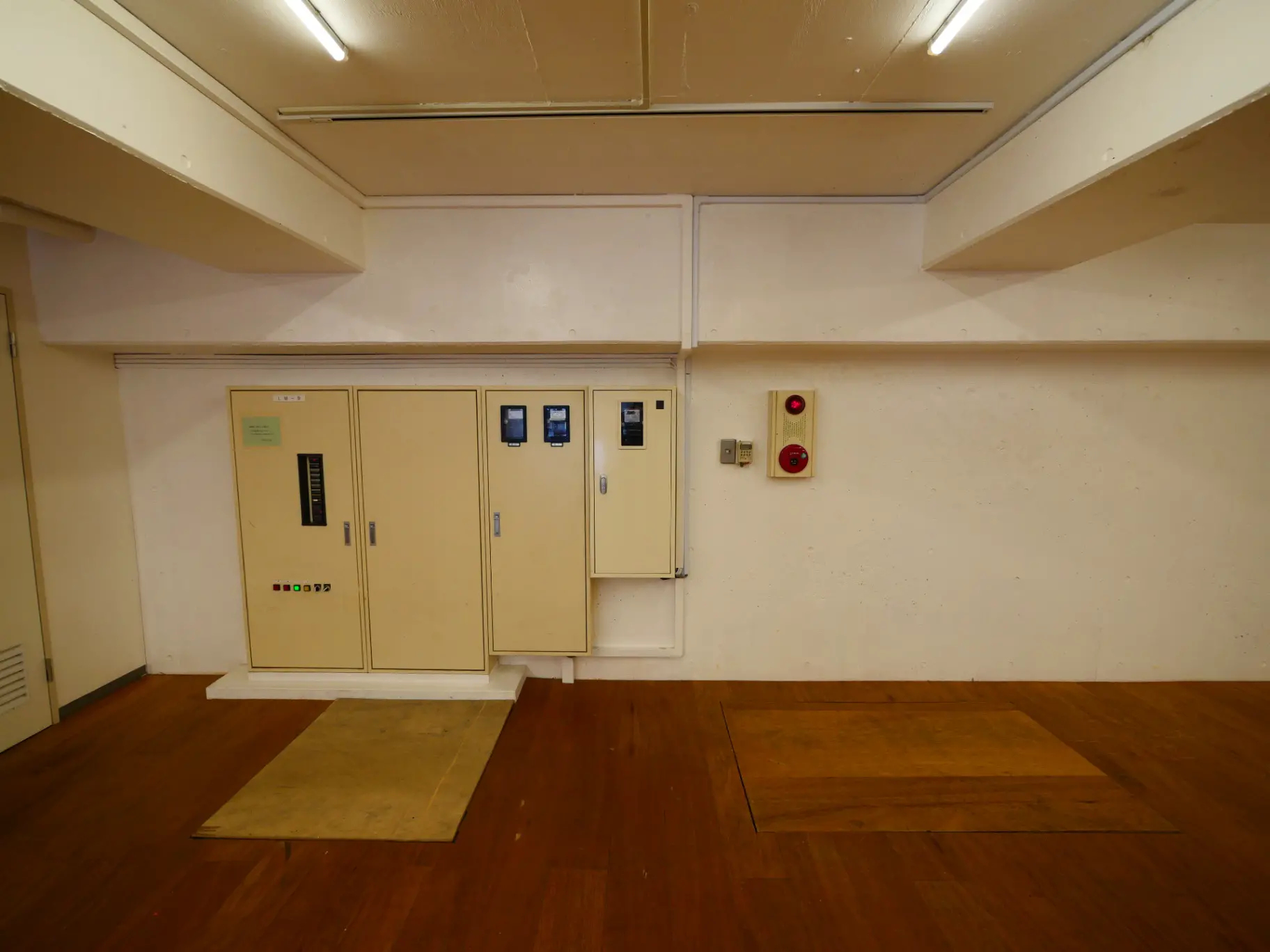 室内の電気設備と分電盤が備え付けられた壁、床に敷かれたマット、シンプルなデザインの部屋