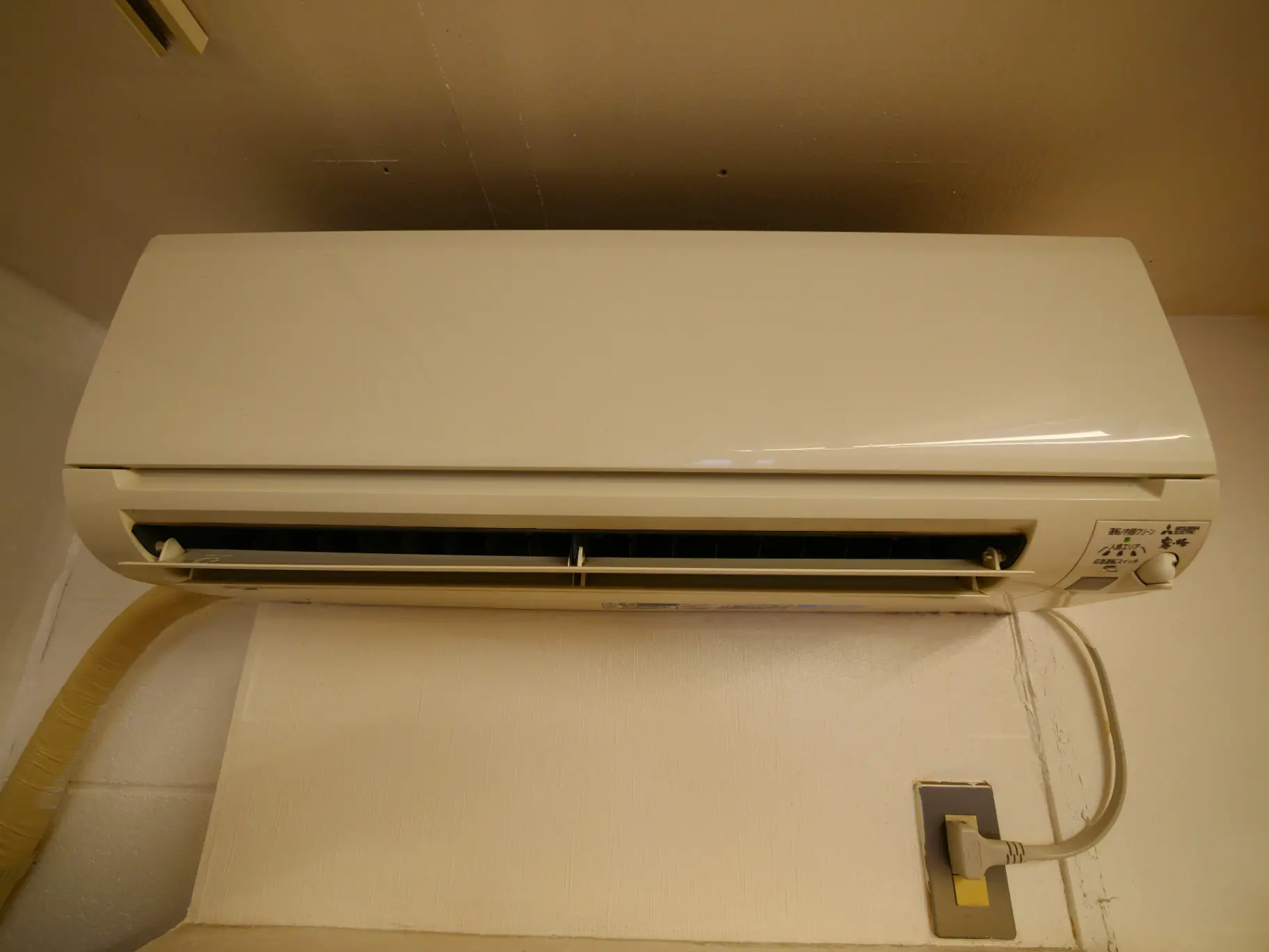壁に取り付けられたホワイトのエアコン、電源プラグと排気ホースが見える室内設備
