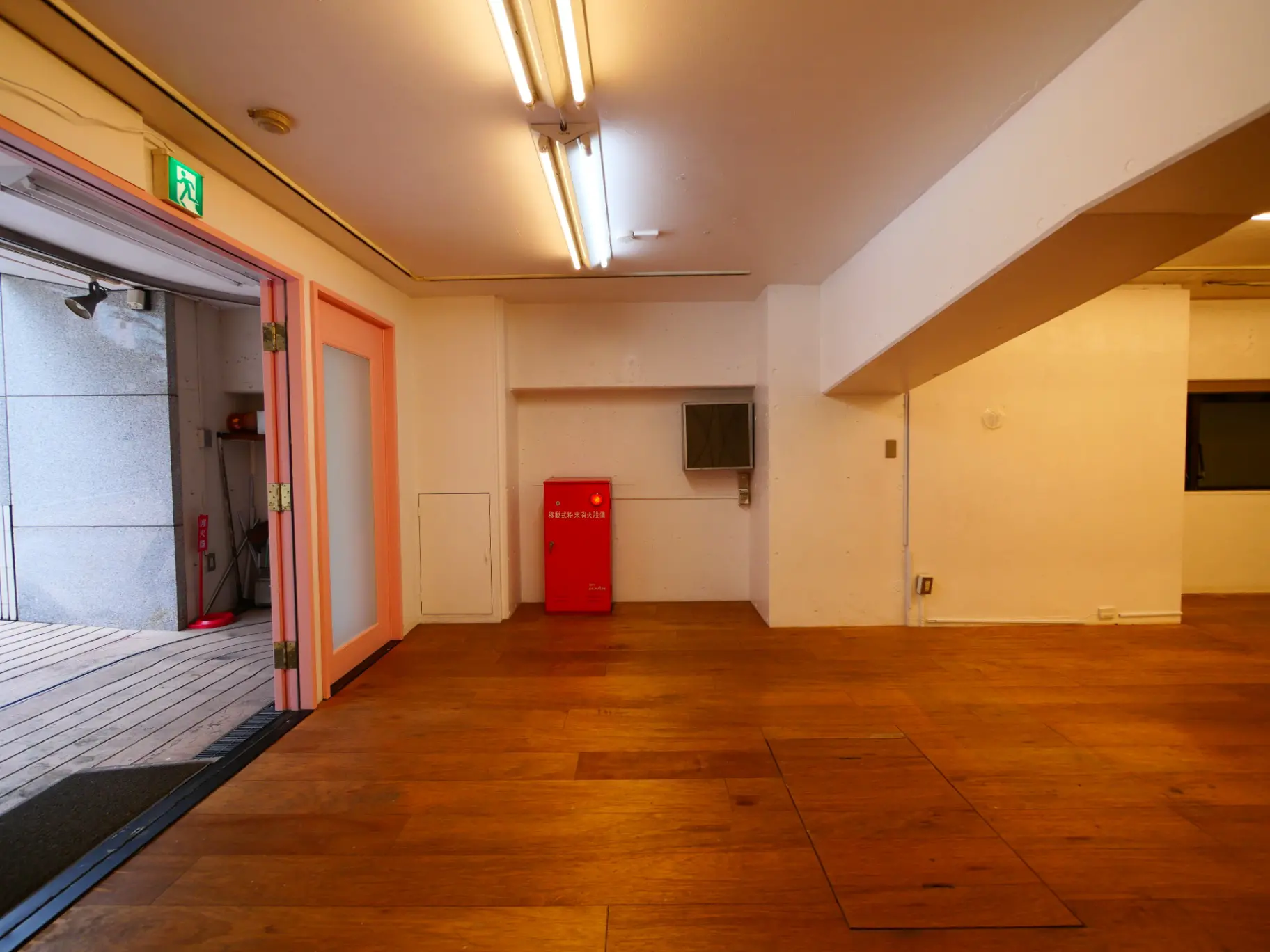 広々としたオフィススペース、木製フローリング、白い壁、フルオープンの出入り口と照明が設置されたインテリア